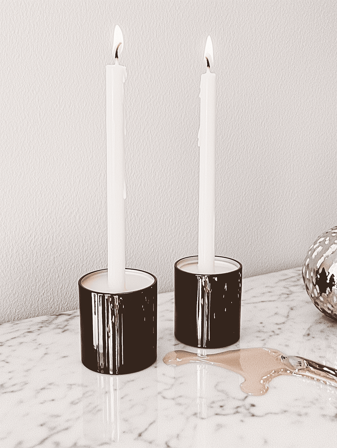 Two lit white candles in dark ceramic holders on a marble table